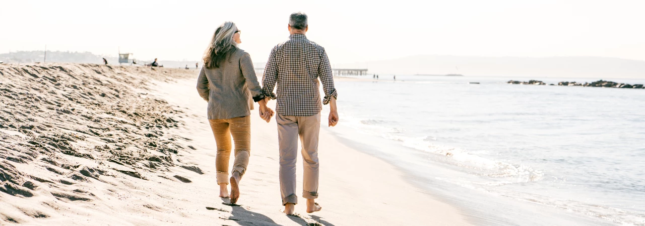a retired couple walking down the beach on a sunny day